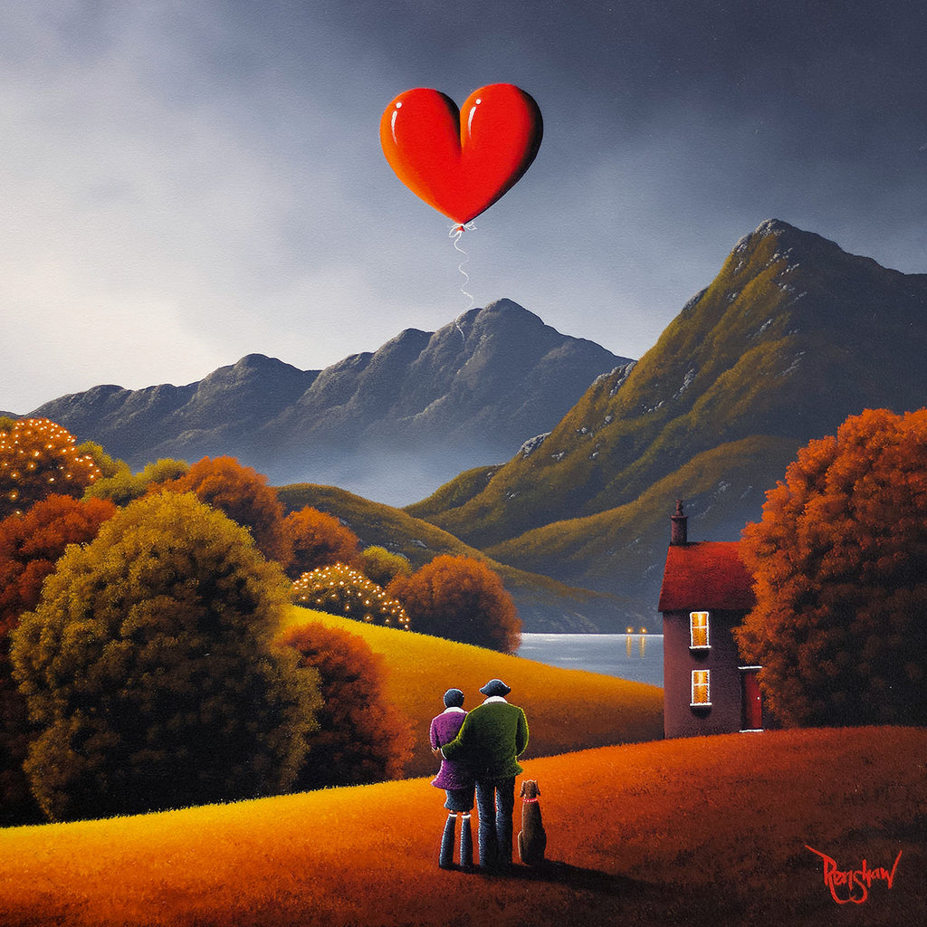 Two people standing on a hill with a red heart-shaped balloon, surrounded by mountains and trees.