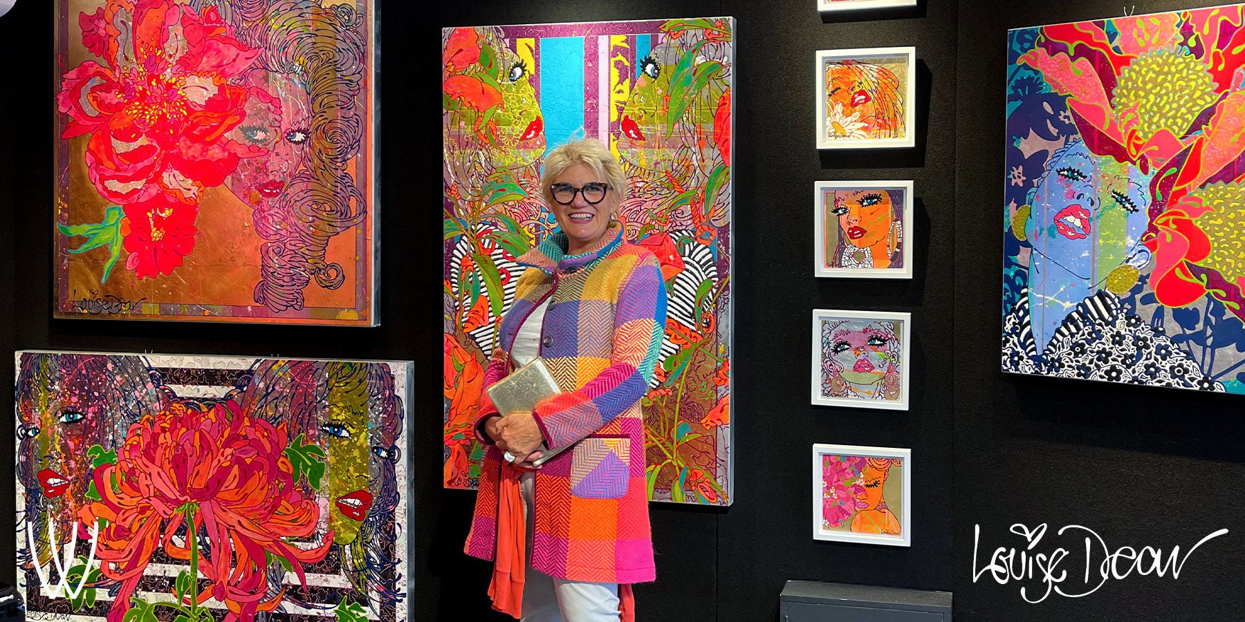 Artist Louise Dear standing in front of a colourful display of her latest paintings in wyecliffe art gallery.