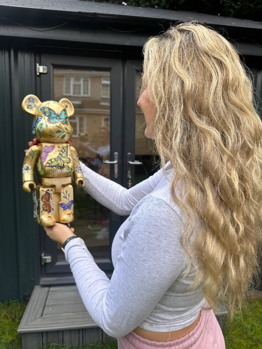 Artist Becky Smith holding her decorative teddy bear sculpture in front of her studio doors.